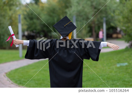 Back view of happy caucasian woman in graduate gown holding diploma outdoors. Back view of happy caucasian woman in graduate gown holding diploma outdoors. 105516264