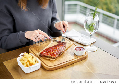 Lunch in a restaurant, a woman cuts Delicious Pork ribs. Full rack of ribs BBQ on wooden plate with french fries and salad 105517394