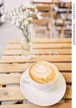 Cup of hot cappuccino. The table in the coworking space of the coffee shop. A cup of coffee on the veranda on a sunny day. Coffee break at the cafe. Close-up Cup of hot cappuccino. The table in the coworking space of the coffee shop. A cup of coffee on the veranda on a sunny day. Coffee break at the cafe. Close-up 105517433