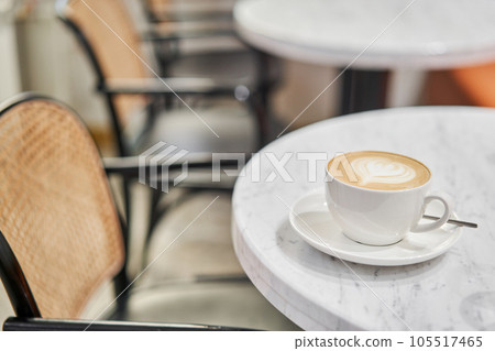 A cup of hot cappuccino on the table in the coworking space of the coffee shop. A cup of coffee on the veranda on a sunny day. Coffee break at the cafe. Close-up 105517465