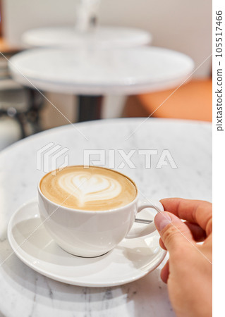 A man holds a cup with his hand A cup of hot cappuccino on the table in the coworking space of the coffee shop. Coffee break at the cafe. Close-up 105517466