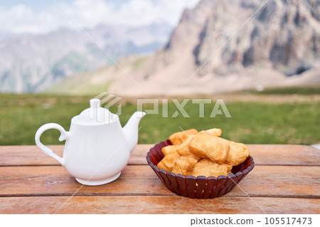 Teapot with tea and delicious National Kazakh pastries baursak. Street cafe in the highlands with a view of the mountains.. Fry dough in boiling oil in a frying pan. 105517473