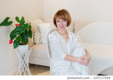 Smiling stylish mature middle aged woman sitting on chair at home in living room and resting. 105517899