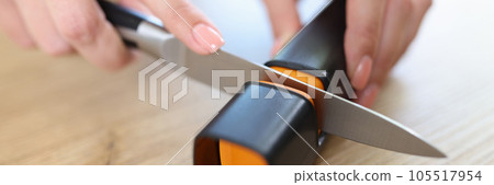 Woman sharpens knife with sharpener in kitchen close-up. 105517954