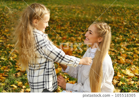 Family spend time together in autumn park. Mother and daughter picking a bouquet of yellow leaves Family spend time together in autumn park. Mother and daughter picking a bouquet of yellow leaves 105518305