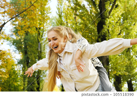 Play, flying or mother with girl on back in autumn park bonding, quality time and playing outdoors. Love, airplane and happy mom piggyback with child on weekend. 105518390