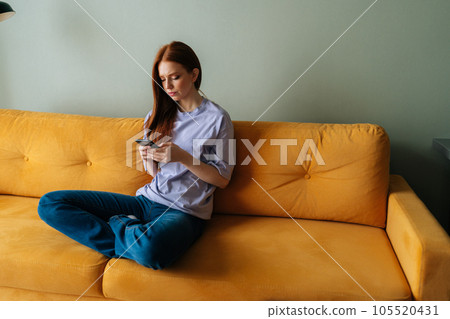 Portrait of frustrated young woman sitting on yellow couch looking at smartphone screen thinking about problem difficulty, feeling failure and exhausted, suffering grief and bad relationship Portrait of frustrated young woman sitting on yellow couch looking at smartphone screen thinking about problem difficulty, feeling failure and exhausted, suffering grief and bad relationship 105520431