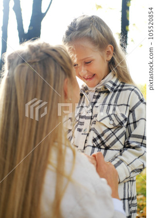 Mother and daughter spend time together in the autumn park. Daughter lovingly looks at mother and laughs Mother and daughter spend time together in the autumn park. Daughter lovingly looks at mother and laughs 105520854