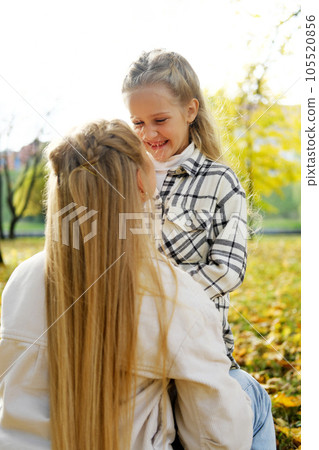 Mother and daughter spend time together in the autumn park. Daughter lovingly looks at mother 105520856
