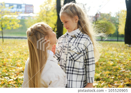 Mother and daughter spend time together in the autumn park. Mother lovingly looks at her daughter Mother and daughter spend time together in the autumn park. Mother lovingly looks at her daughter 105520905