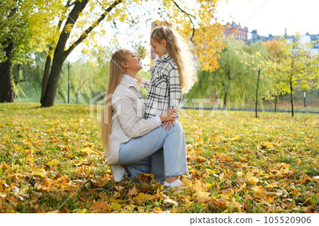 Mother and daughter spend time together in the autumn park. Mother lovingly looks at her daughter Mother and daughter spend time together in the autumn park. Mother lovingly looks at her daughter 105520906