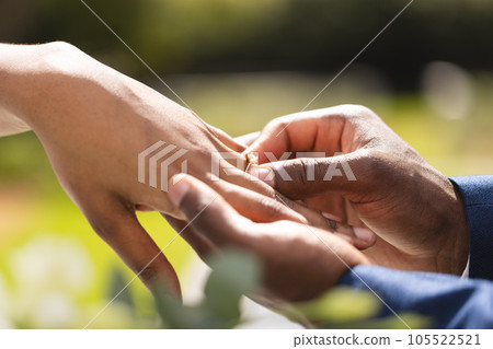 Hands of african american bride and groom placing ring on finger at wedding ceremony in sunny garden Hands of african american bride and groom placing ring on finger at wedding ceremony in sunny garden 105522521