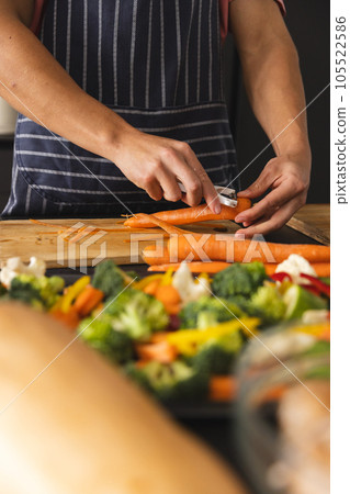 Midsection of biracial man in apron peeling carrot on chopping board, copy space Midsection of biracial man in apron peeling carrot on chopping board, copy space 105522586