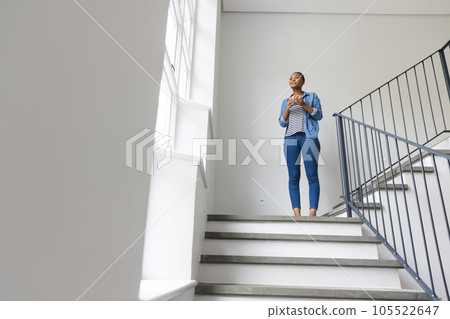 Thoughtful african american woman on staircase, holding coffee and looking out of window, copy space 105522647