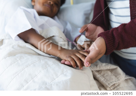 African american girl patient lying on bed holding hands with her mother in patient room at hospital African american girl patient lying on bed holding hands with her mother in patient room at hospital 105522695