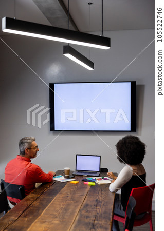 Rear view of diverse man and businesswoman discussing over a laptop and tv with copy space at office 105522746