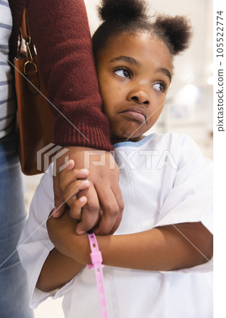 Sad african american girl patient and her mother holding hands in corridor at hospital Sad african american girl patient and her mother holding hands in corridor at hospital 105522774