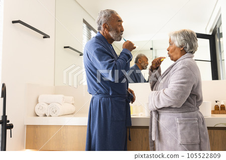Happy senior biracial couple wearing bathrobes and brushing teeth in bathroom at home 105522809