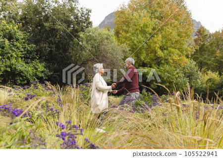 Happy senior biracial couple dancing with flowers around them in garden at home 105522941
