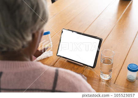 Senior biracial woman having video call with doctor on tablet with copy space, holding pills at home 105523057