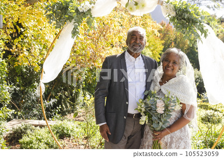 Portrait of happy senior biracial bride and groom at sunny outdoor wedding ceremony Portrait of happy senior biracial bride and groom at sunny outdoor wedding ceremony 105523059