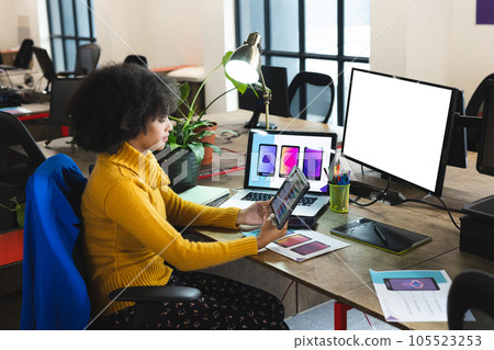 Focused african american female designer using tablet and computer with copy space at desk in office Focused african american female designer using tablet and computer with copy space at desk in office 105523253