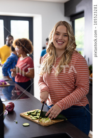Portrait of happy caucasian woman cutting vegetables with diverse friends in kitchen 105523281