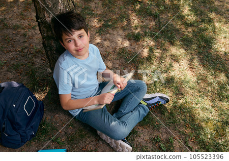 View from above of a school kid, adorable preteen boy in casual denim, reading book after school in the backyard 105523396