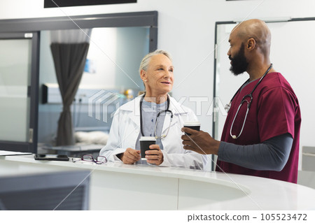 Diverse male and female doctors talking and drinking coffee in reception at hospital 105523472