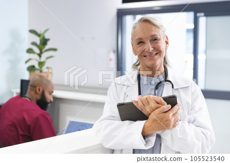 Portrait of happy senior caucasian female doctor holding tablet in reception at hospital 105523540