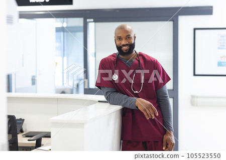 Portrait of happy african american male doctor wearing scrubs in reception at hospital 105523550