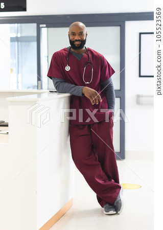 Portrait of happy african american male doctor wearing scrubs in reception at hospital 105523569