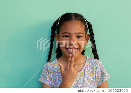 Biracial schoolgirl doing sign language gestures over blue background at elementary school 105523623