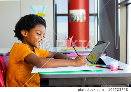 Happy biracial schoolboy having lesson on tablet video call in classroom Happy biracial schoolboy having lesson on tablet video call in classroom 105523728