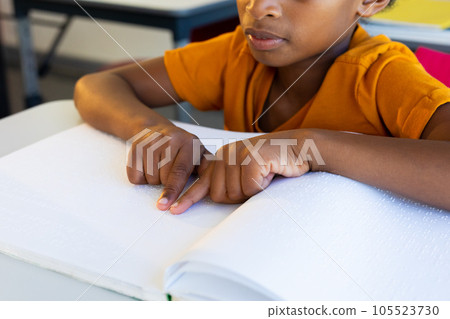 Focused biracial schoolboy reading braille with hands in classroom 105523730