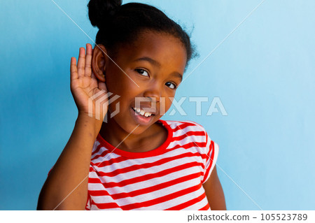 Portrait of happy african american schoolgirl doing gesture of listening over blue background Portrait of happy african american schoolgirl doing gesture of listening over blue background 105523789