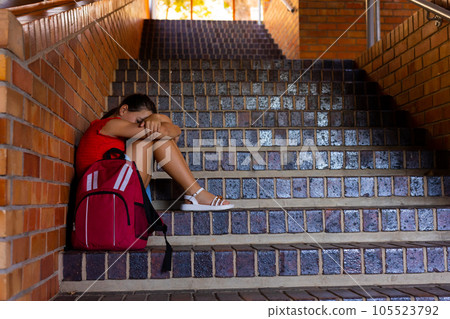 Sad caucasian schoolgirl with school bag sitting on stairs at school, copy space 105523792
