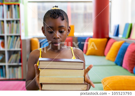 Shocked african american schoolgirl holding books over couch with colourful pillows 105523793
