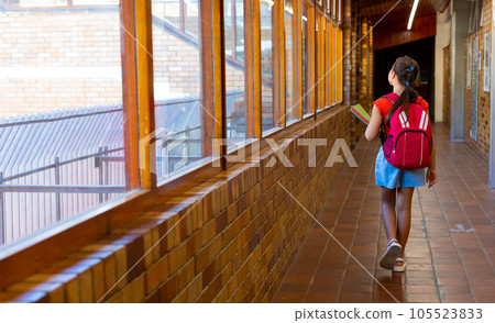 Caucasian schoolgirl walking with school bag and books at school corridor, copy space 105523833