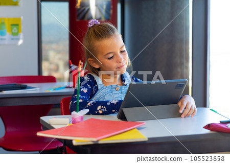 Happy caucasian schoolgirl sitting at desk and learning during tablet video call Happy caucasian schoolgirl sitting at desk and learning during tablet video call 105523858