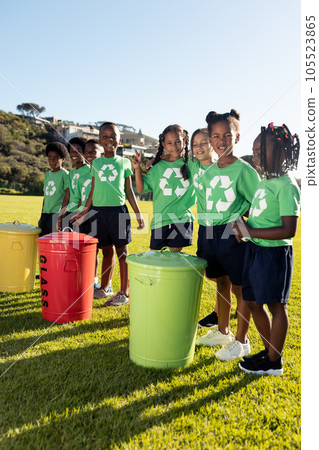 Portrait of happy diverse children collecting recycling embracing in sunny elementary school field 105523865