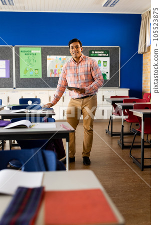 Happy biracial male teacher with tablet in elementary school classroom, copy space Happy biracial male teacher with tablet in elementary school classroom, copy space 105523875