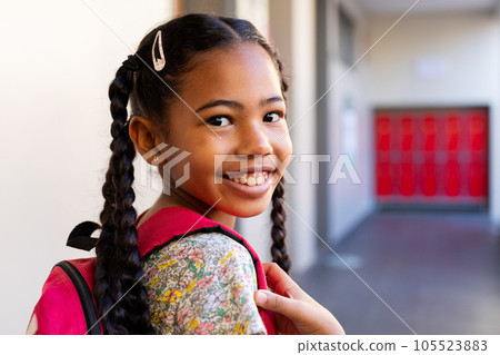 Portrait of happy biracial schoolgirl with school bag in corridor at elementary school 105523883