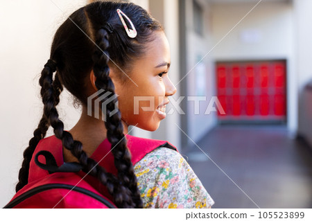Happy biracial schoolgirl walking with school bag in corridor at elementary school 105523899