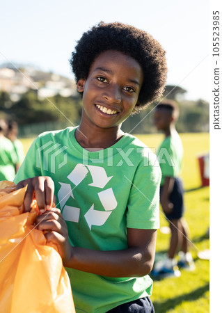 Portrait of happy african american schoolboy collecting recycling in sunny elementary school field 105523985
