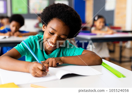Portrait of happy african american elementary schoolboy writing in notebook at desk in class Portrait of happy african american elementary schoolboy writing in notebook at desk in class 105524056