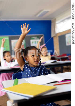 Diverse elementary schoolchildren sitting at desks and raising hands in class Diverse elementary schoolchildren sitting at desks and raising hands in class 105524206