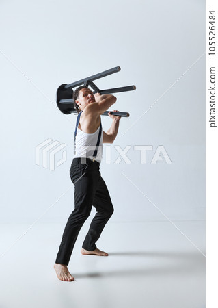 Portrait of handsome mature man with muscular body posing with chair against grey studio background. Emotions 105526484