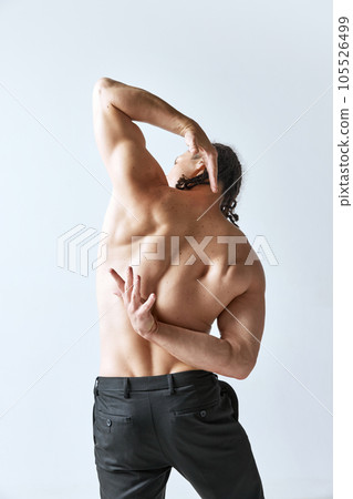 Rear view image of shirtless man posing in black pants against grey studio background. Relieve, muscular body Rear view image of shirtless man posing in black pants against grey studio background. Relieve, muscular body 105526499