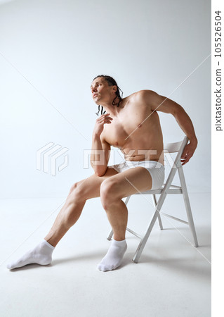 Handsome, stylish mature man posing shirtless in underwear, sitting on chair against grey studio background. Muscular body 105526504